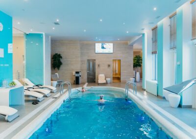 Luxurious indoor swimming pool in a modern spa with lounge chairs and soft lighting.